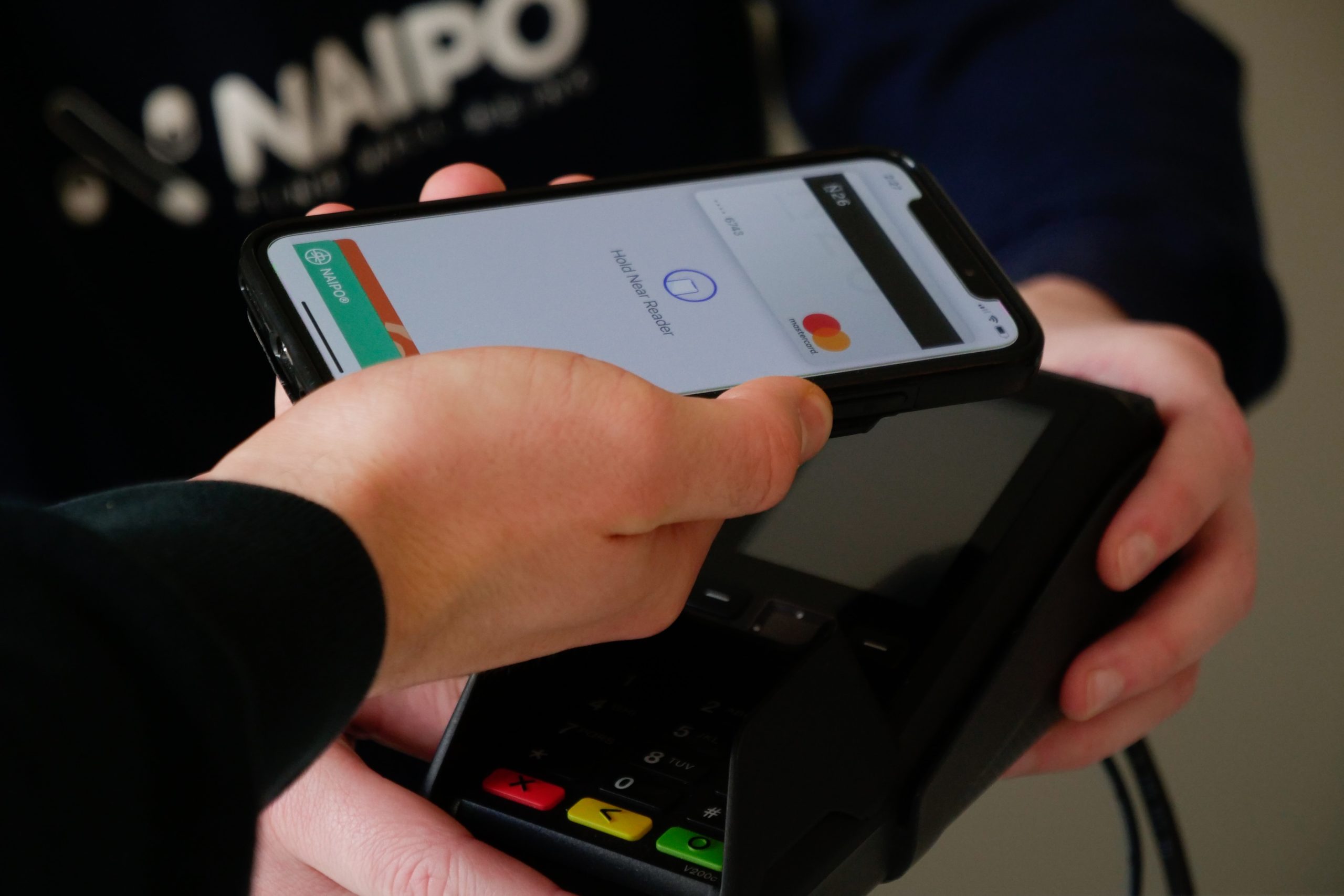 person holding a black phone with card tap feature to pay for a transaction